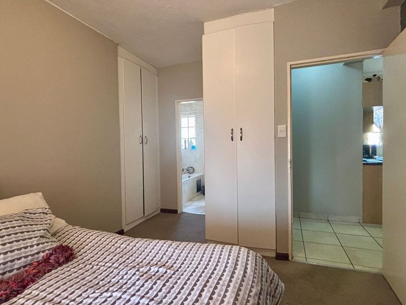 Bedroom featuring built-in cupboards, neutral wall finishes, and direct access to an adjoining bathroom and hallway area.