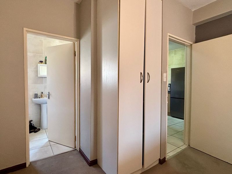 A functional hallway featuring built-in cupboards, providing access to a bathroom and kitchen area with neutral wall finishes.