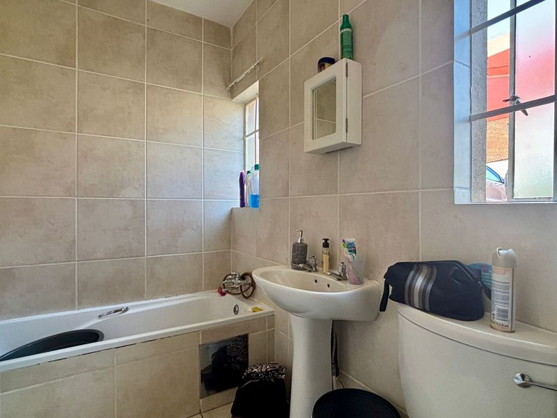 A functional bathroom featuring a bathtub, pedestal basin, and toilet with neutral wall tiling and natural light from two windows.