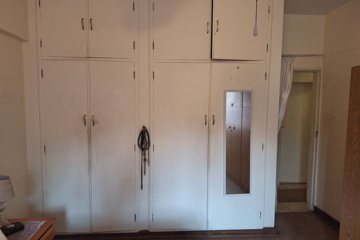 Bedroom featuring floor-to-ceiling built-in cupboards with an integrated mirror and overhead storage compartments.