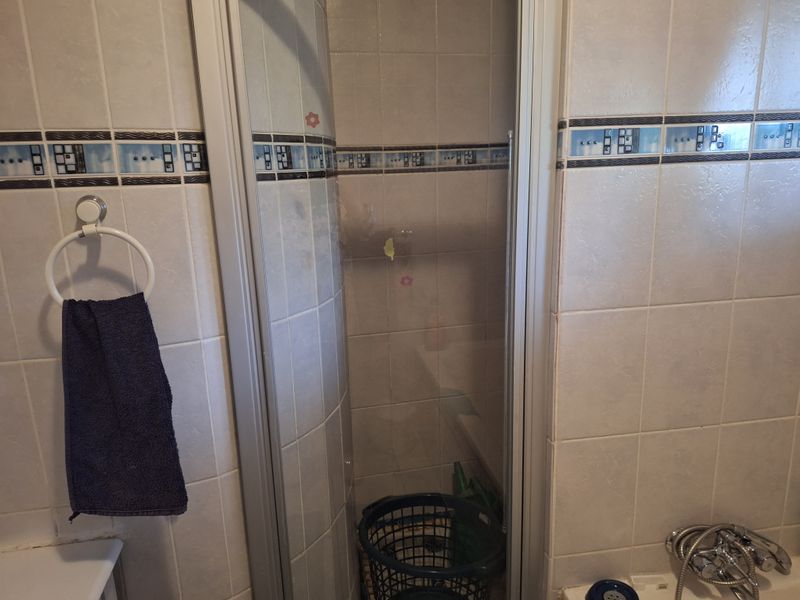A dated bathroom featuring a shower enclosure with tiled walls and a bathtub faucet.