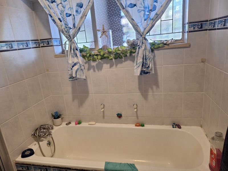 A functional bathroom featuring a built-in bathtub with wall-mounted mixer taps and classic ceramic wall tiling.