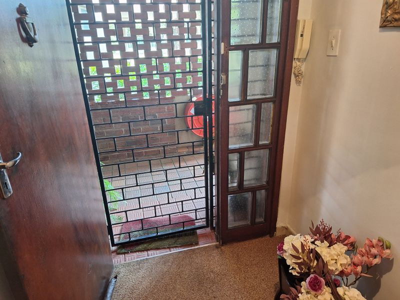 Entrance area featuring a timber door, security gate, and intercom system, leading out to a private brick-screened patio space.