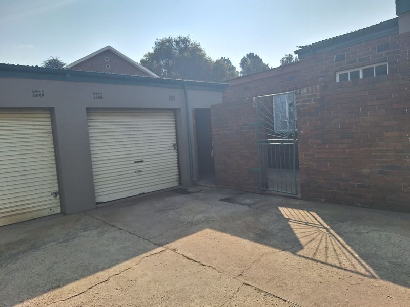 Rear exterior view of the property featuring a double garage with roller doors, brick masonry walls, and a paved driveway area.