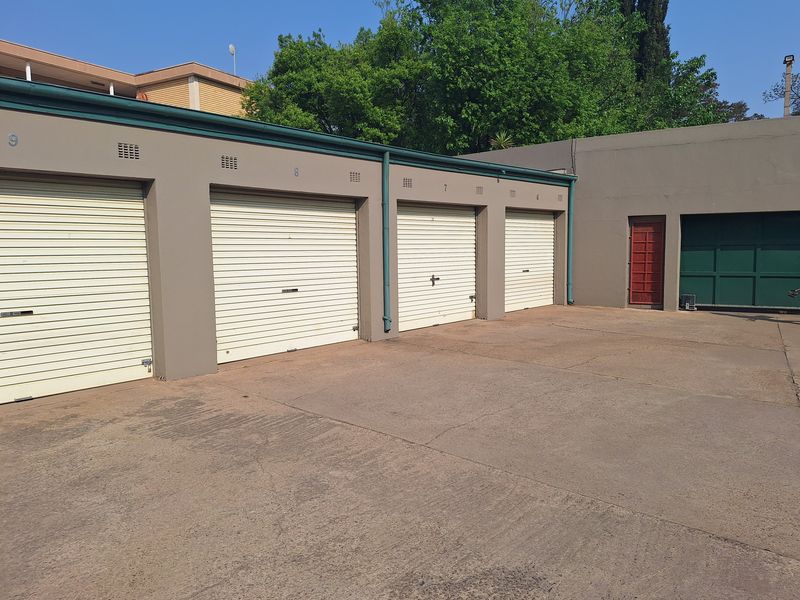 A row of four secure garage units with roller shutter doors and a shared concrete driveway area.