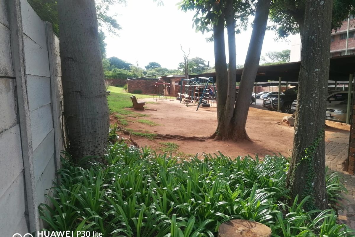 Outdoor communal area featuring a playground, mature trees, and covered parking bays within the property grounds.