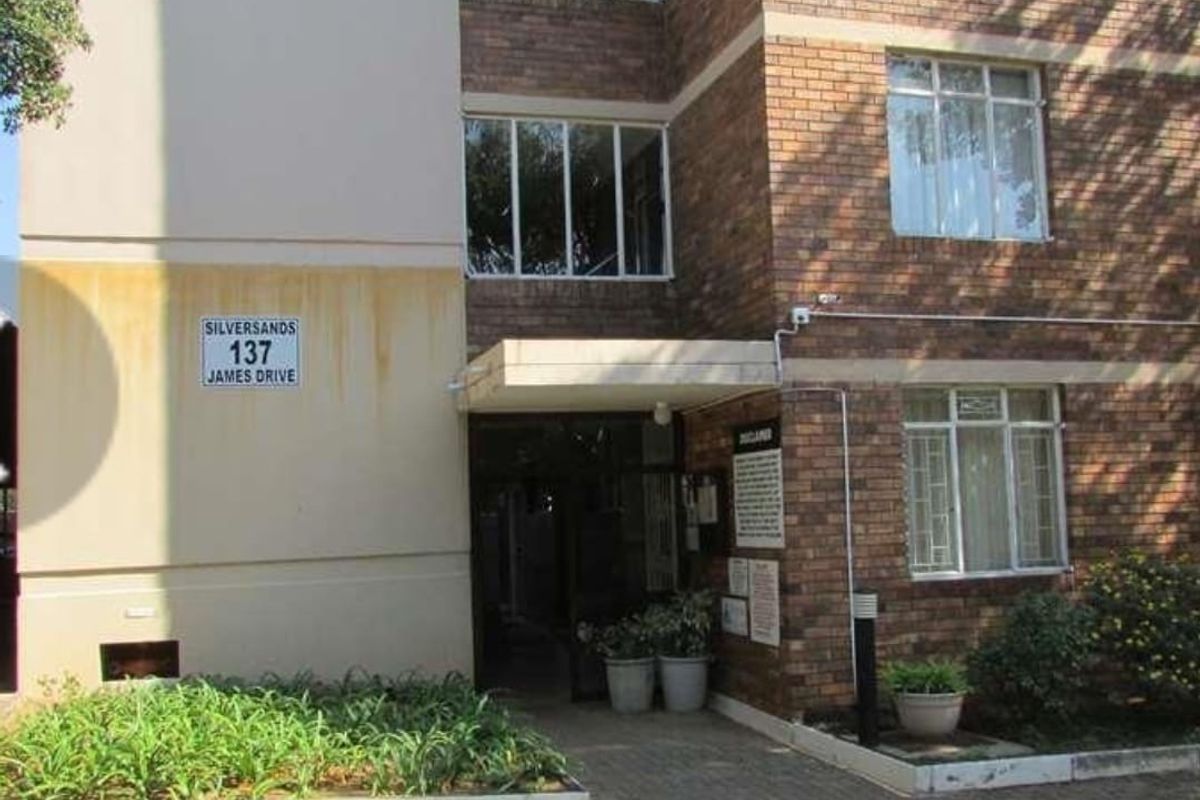 Exterior view of the Silversands apartment building entrance, featuring face-brick facade, paved walkway, and established garden beds.