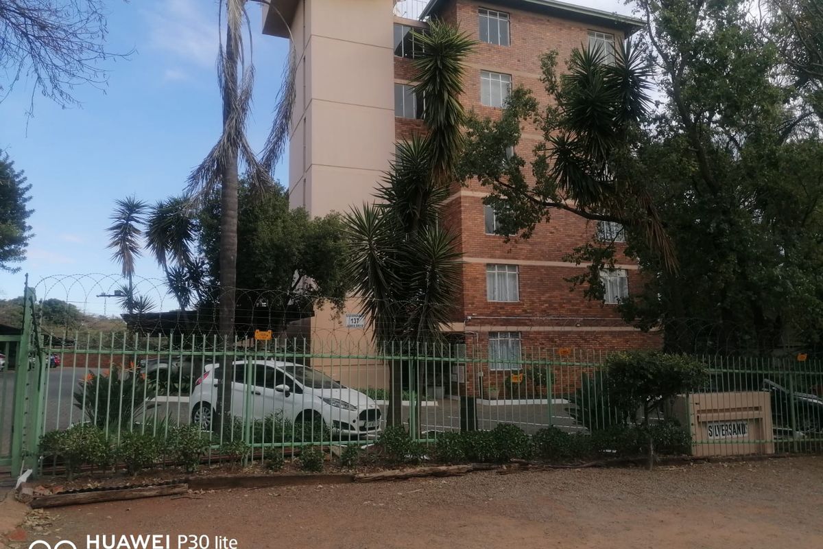 Exterior view of the Silversands apartment building, featuring a multi-story brick facade, secure perimeter fencing, and established trees.