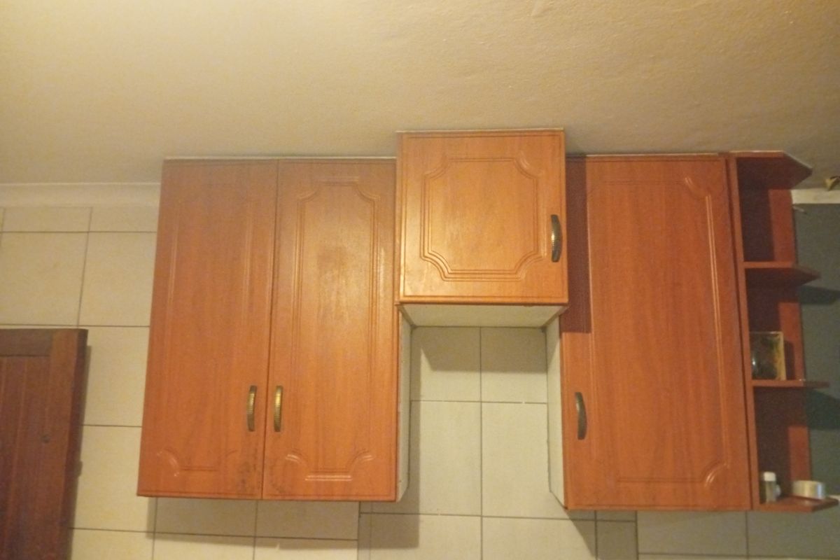 A close-up view of dated wall-mounted kitchen cabinetry with wood-look finish and tiled splashback.
