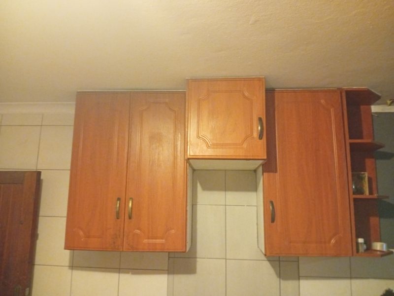 A close-up view of dated wall-mounted kitchen cabinetry with wood-look finish and tiled splashback.