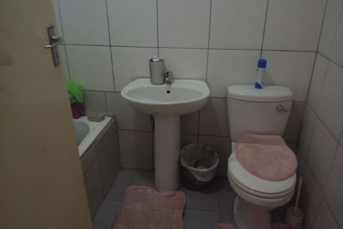 A compact bathroom featuring a pedestal basin, toilet, and bathtub with full-height wall tiling.