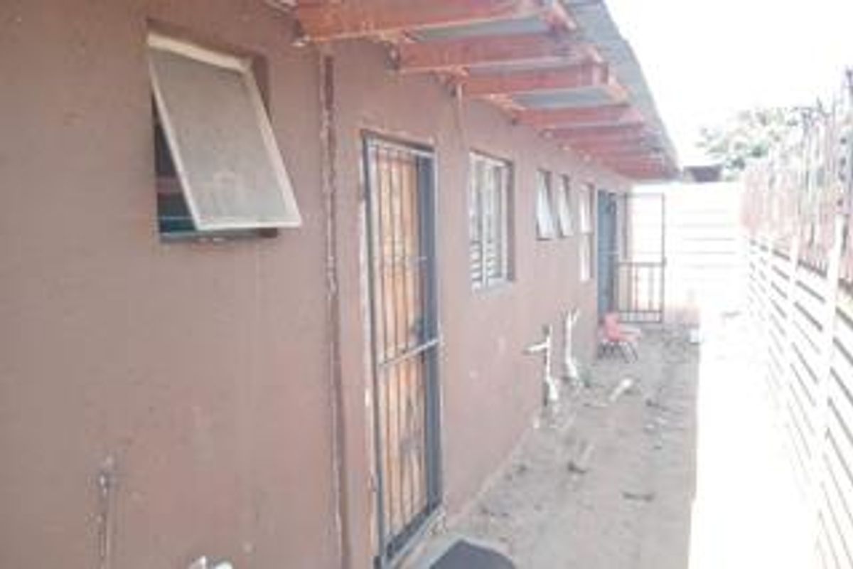Side exterior view of the property featuring a narrow walkway, security gates, and exposed roof structure along the building facade.