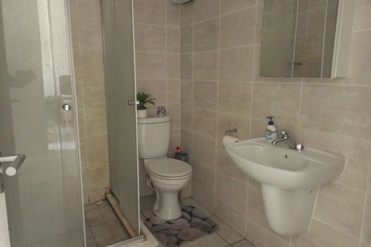 A functional bathroom featuring a shower enclosure, pedestal basin, toilet, and neutral wall and floor tiling.