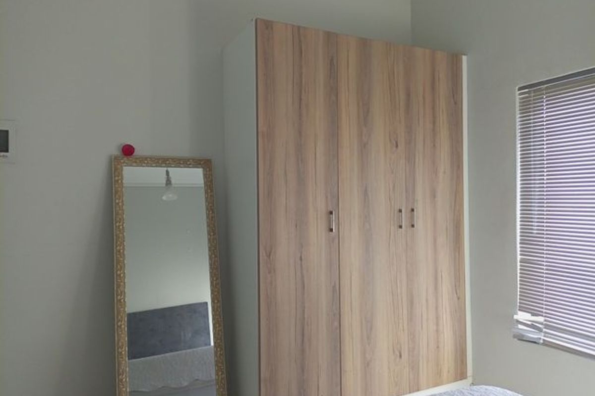 A bedroom featuring a modern wood-finish built-in wardrobe and venetian blinds, providing clean and functional storage space.