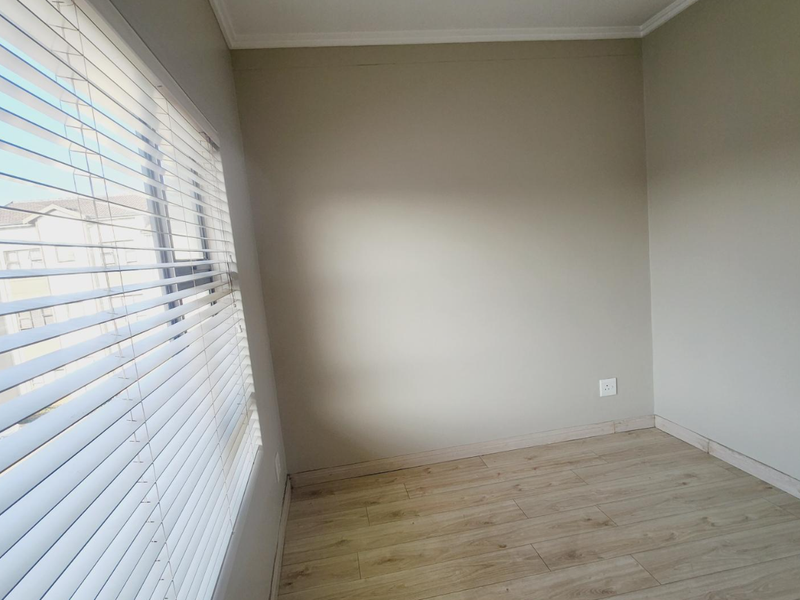 A bright, empty bedroom featuring light wood-look laminate flooring, neutral wall tones, and fitted venetian blinds.