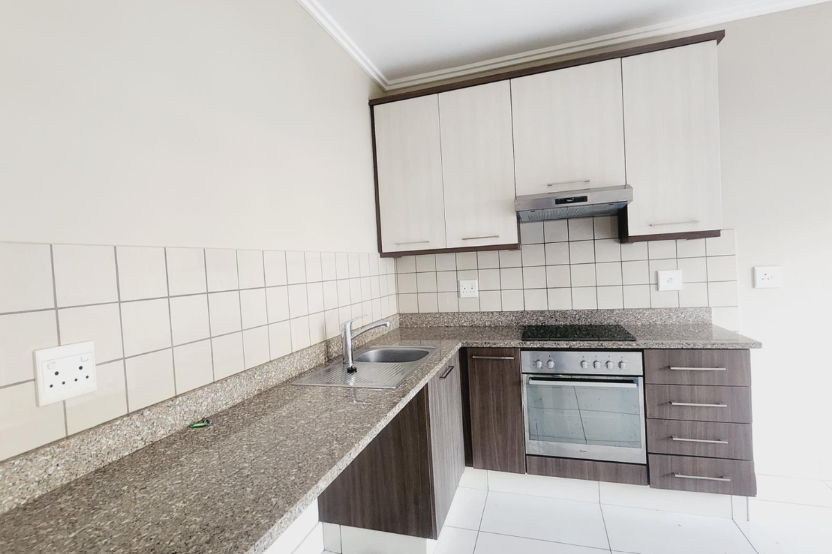 Modern kitchen featuring granite countertops, built-in oven, electric hob, extractor fan, and two-tone cabinetry with tiled splashbacks.