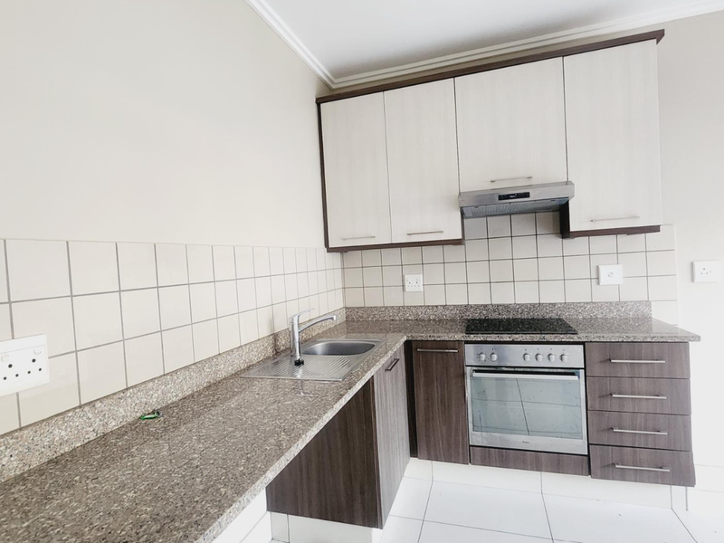 Modern kitchen featuring granite countertops, built-in oven, electric hob, extractor fan, and two-tone cabinetry with tiled splashbacks.