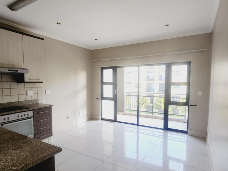 Open-plan kitchen and living area featuring tiled flooring, built-in cabinetry, integrated oven and hob, and sliding glass doors leading to a private balcony.