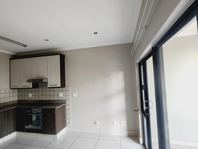 Modern open-plan kitchen featuring dark and light cabinetry, granite countertops, built-in oven, hob, and extractor fan, with direct access to a balcony.