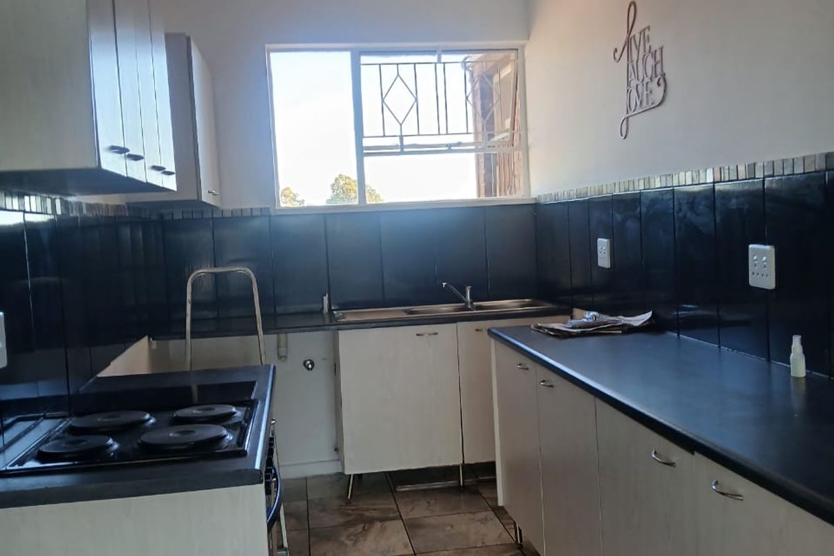 A functional kitchen featuring white cabinetry, dark countertops, black tiled splashbacks, and a built-in electric hob.