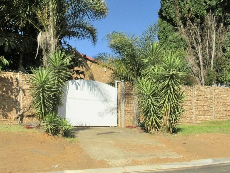 Front view of the property featuring a solid driveway gate, brick boundary wall, and established garden landscaping.