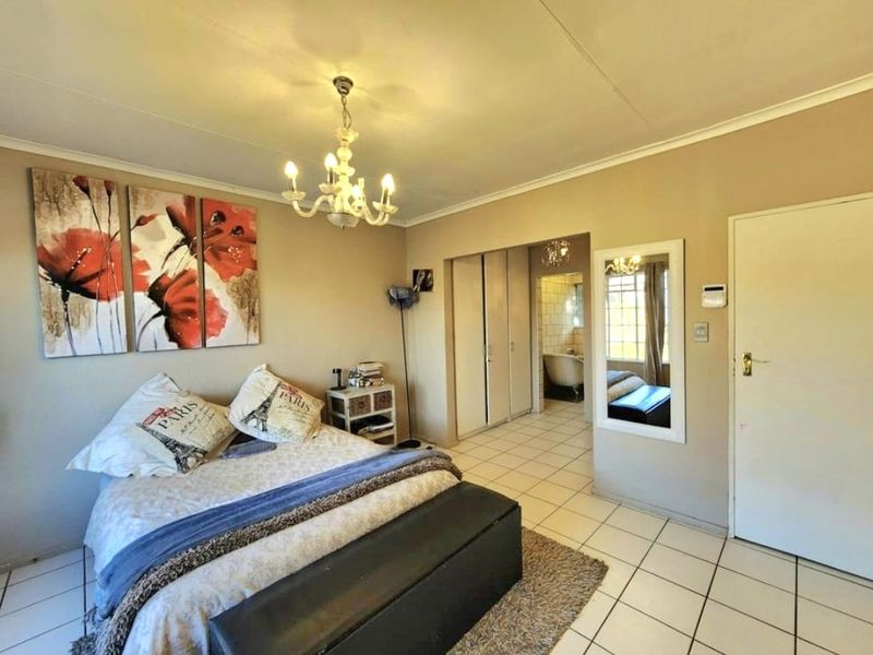 Spacious bedroom featuring tiled flooring, built-in cupboards, and direct access to an en-suite bathroom with a classic chandelier fixture.