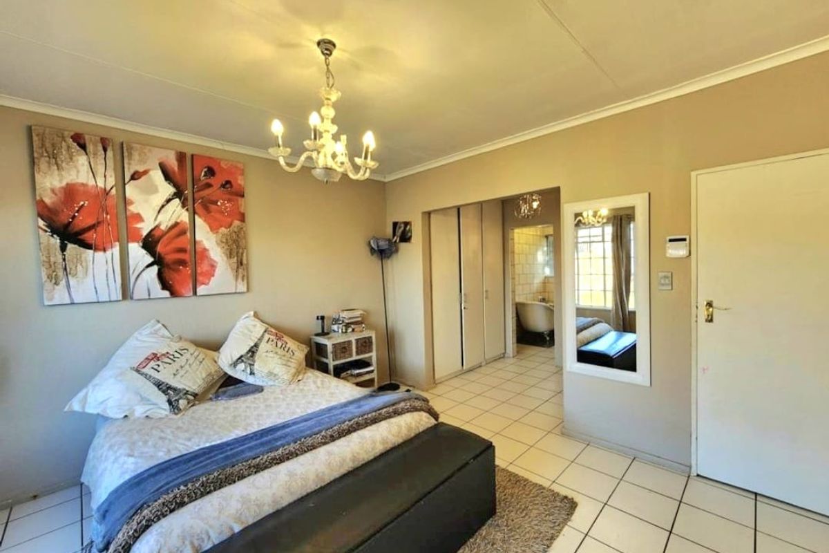 Spacious bedroom featuring tiled flooring, built-in cupboards, and direct access to an en-suite bathroom with a classic chandelier fixture.