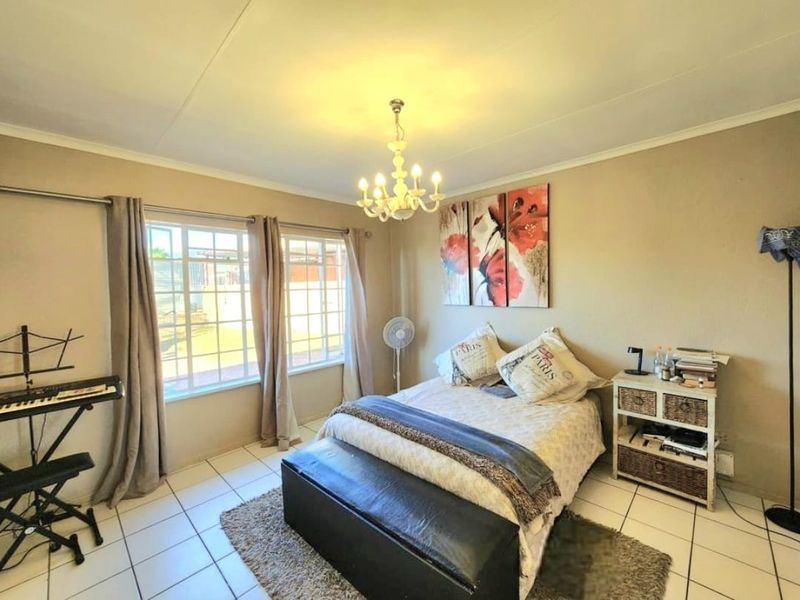 A well-lit bedroom featuring tiled flooring, large windows with security bars, and a central ceiling light fixture.