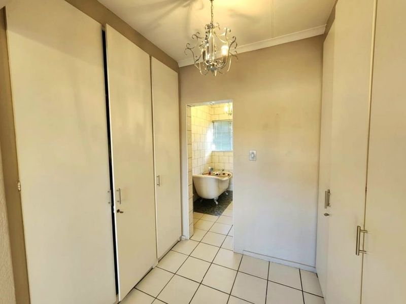 A hallway featuring extensive built-in cupboard storage and tiled flooring, leading directly into a bathroom with a classic clawfoot bathtub.
