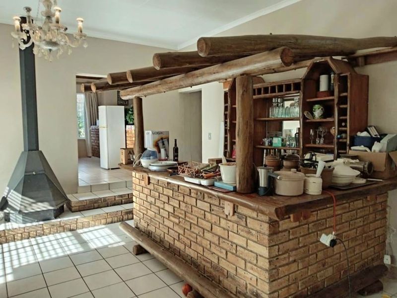 A rustic indoor bar area featuring a brick counter with a timber log canopy and a prominent freestanding fireplace.