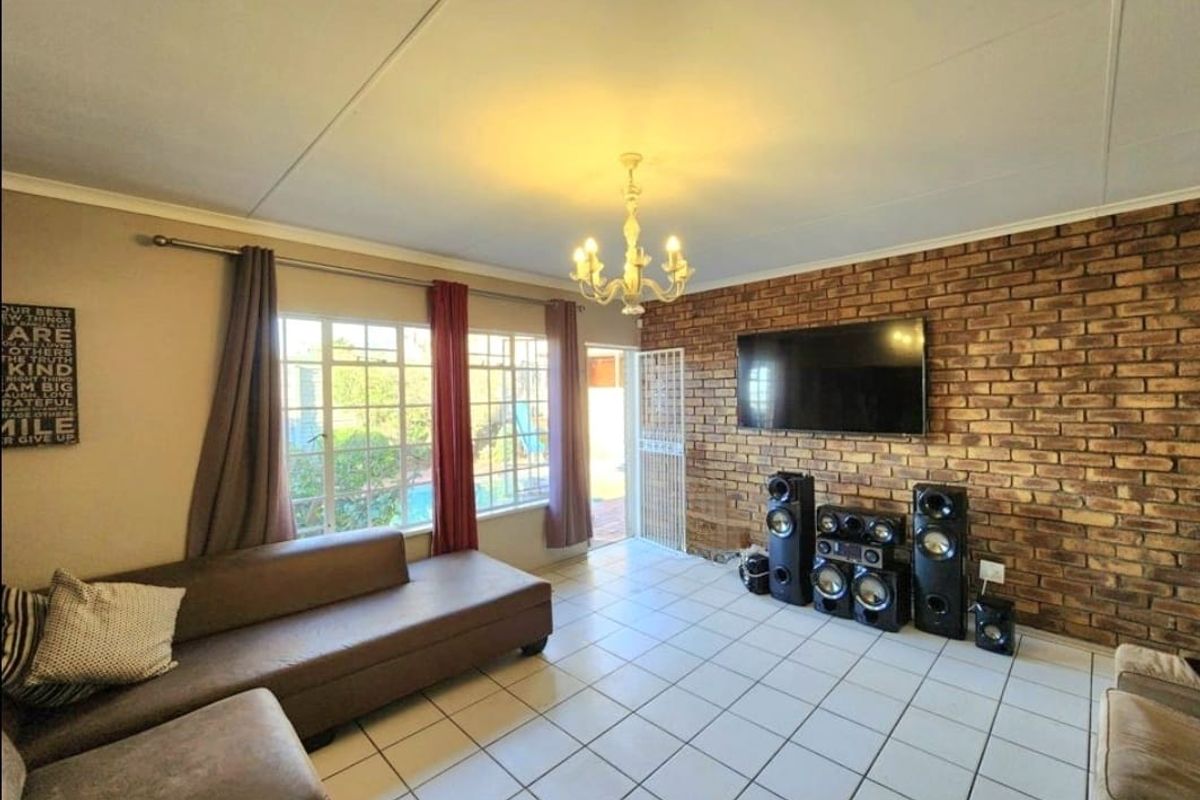 Spacious living room featuring an exposed brick accent wall, ceramic tiled flooring, and direct access to the outdoor patio area.