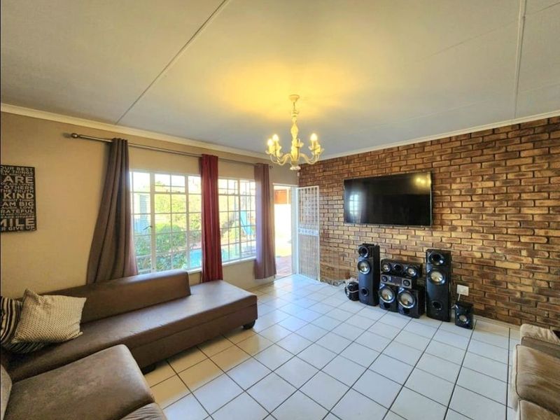 Spacious living room featuring an exposed brick accent wall, ceramic tiled flooring, and direct access to the outdoor patio area.