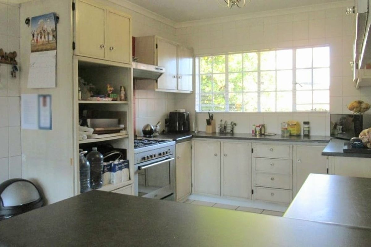 A functional kitchen featuring built-in cabinetry, laminate countertops, a gas stove with extractor fan, and tiled splashbacks, offering potential for modern updates.