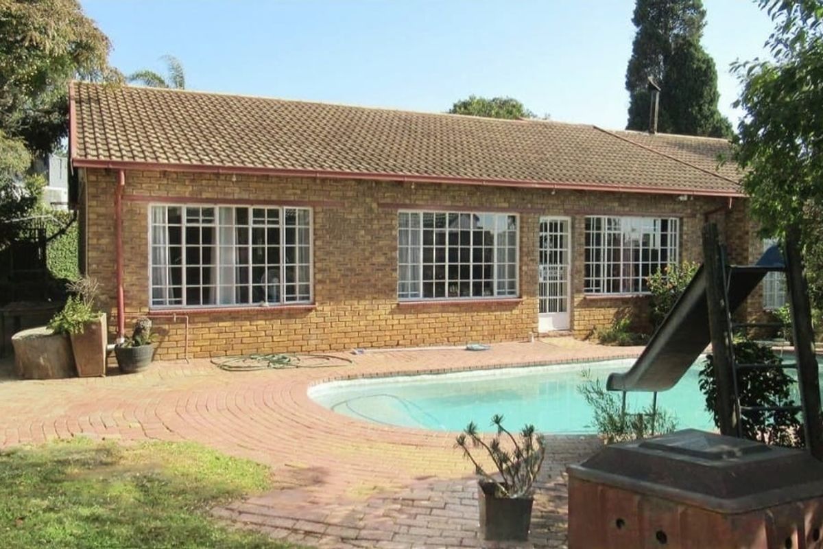 Rear view of the property featuring a facebrick facade, tiled roof, and a swimming pool set within a paved outdoor area.