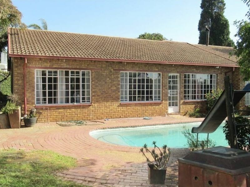 Rear view of the property featuring a facebrick facade, tiled roof, and a swimming pool set within a paved outdoor area.