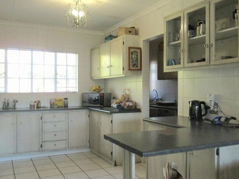 A dated kitchen featuring white built-in cabinetry, tiled backsplash, and a breakfast bar, with an adjacent scullery area visible.