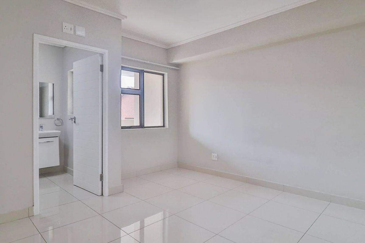 A bright, empty bedroom featuring neutral tiled flooring, clean white walls, and an adjoining en-suite bathroom with modern fixtures.