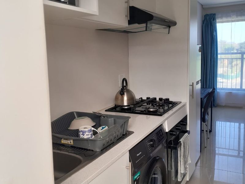 Compact modern kitchen featuring white cabinetry, stone countertops, gas hob, extractor fan, built-in oven, and integrated washing machine with tiled flooring.