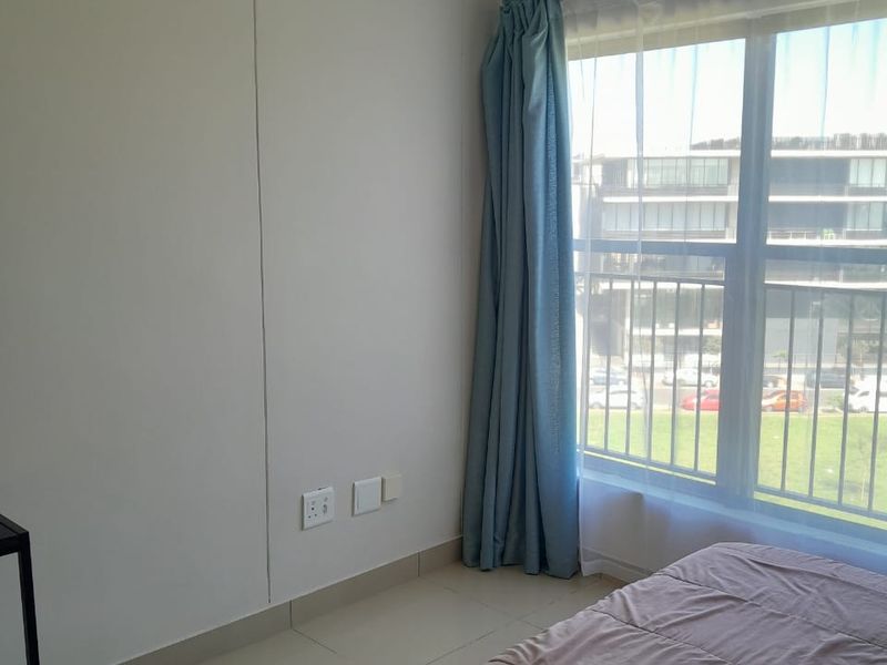 A bright bedroom featuring tiled flooring, neutral walls, and a large window with natural light.