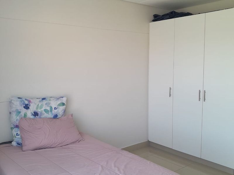 A clean bedroom featuring neutral tiled flooring, a white built-in wardrobe, and a simple ceiling light fixture.