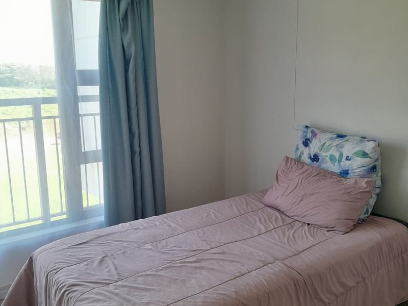 A bright bedroom featuring tiled flooring and a sliding glass door providing access to a balcony with outdoor views.