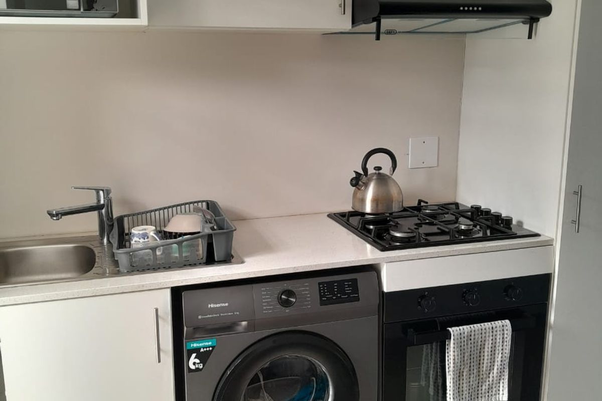Compact modern kitchen featuring white cabinetry, stone countertops, gas hob, built-in oven, extractor fan, and an integrated washing machine.