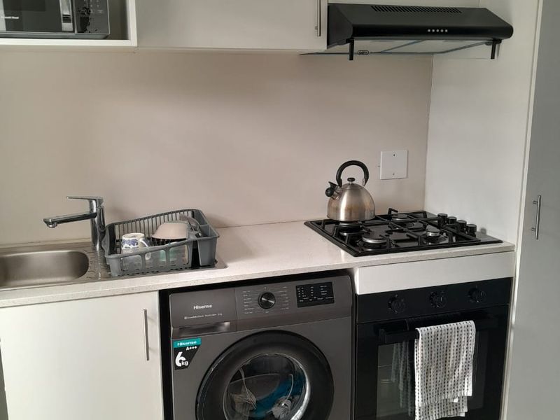 Compact modern kitchen featuring white cabinetry, stone countertops, gas hob, built-in oven, extractor fan, and an integrated washing machine.