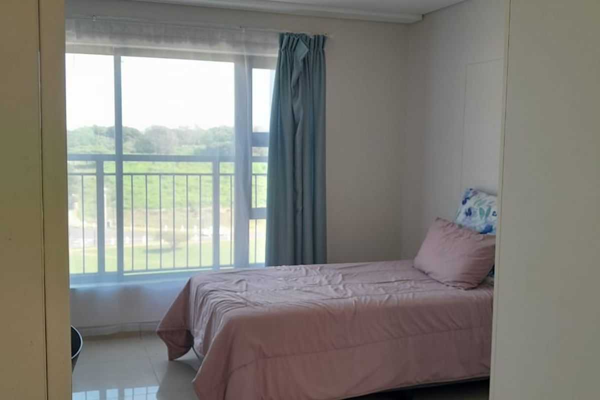 A bright bedroom featuring large windows with natural light, tiled flooring, and access to a balcony with scenic views.