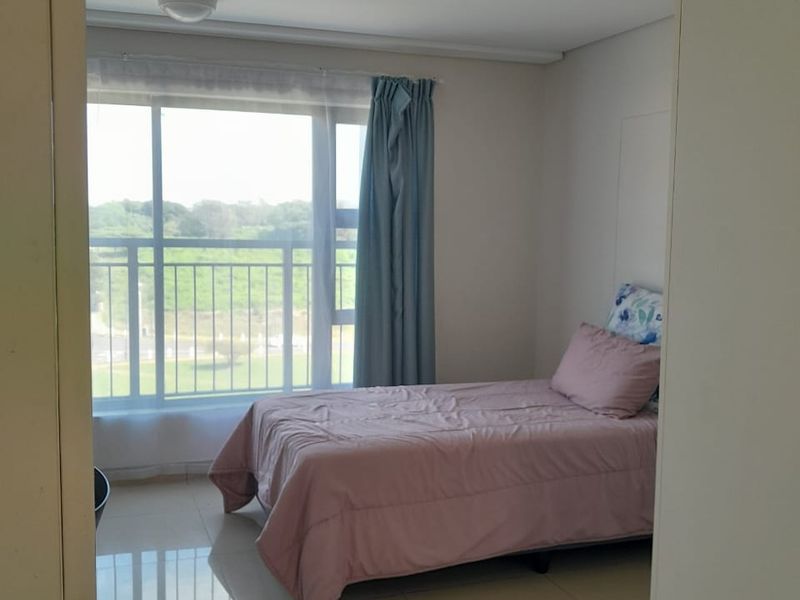 A bright bedroom featuring large windows with natural light, tiled flooring, and access to a balcony with scenic views.