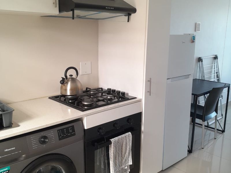 Compact modern kitchen featuring built-in cabinetry, gas hob, electric oven, extractor fan, and stone countertops with tiled flooring.