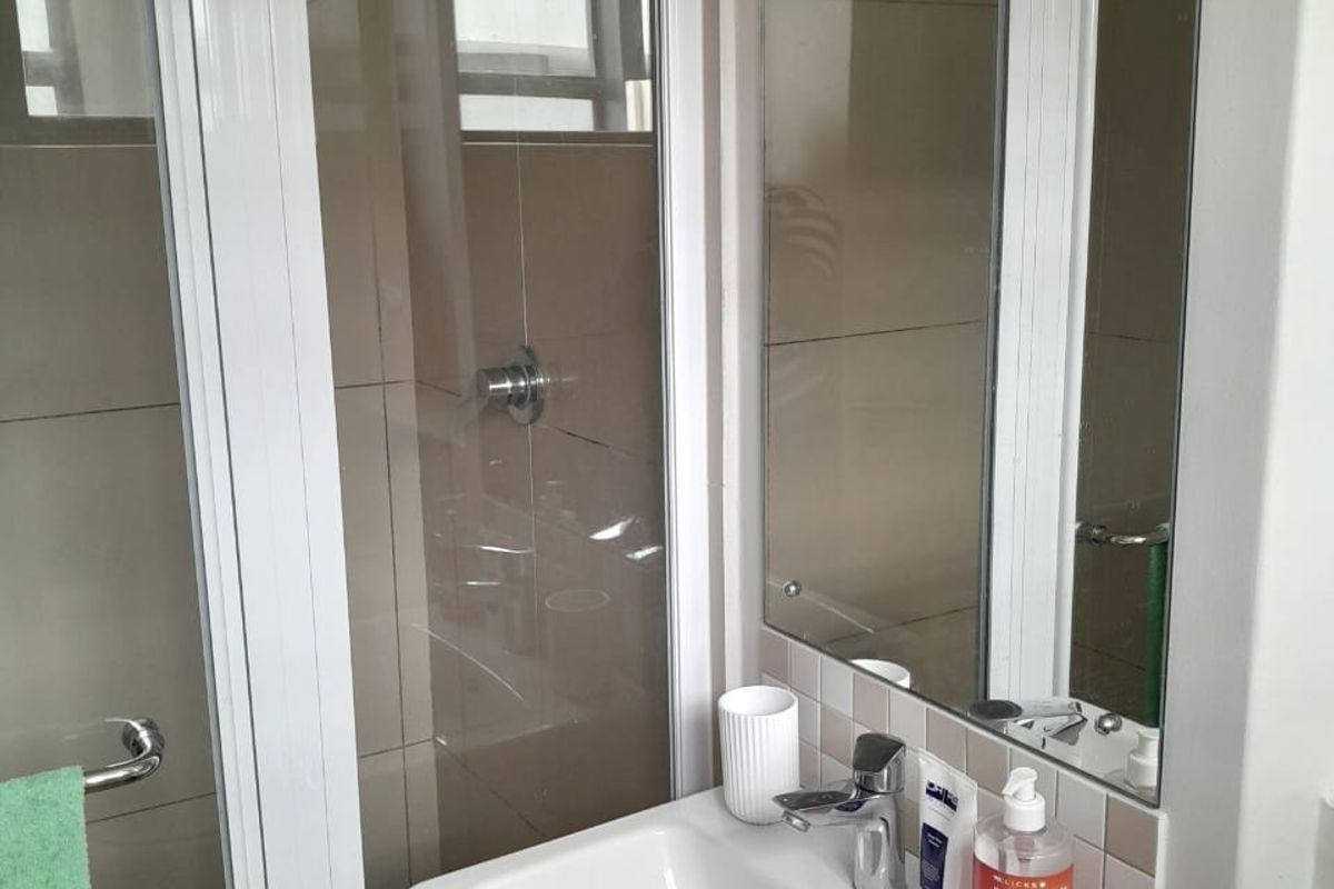 A compact bathroom featuring a wall-mounted basin with a mixer tap, a tiled shower enclosure, and a wall-mounted mirror.