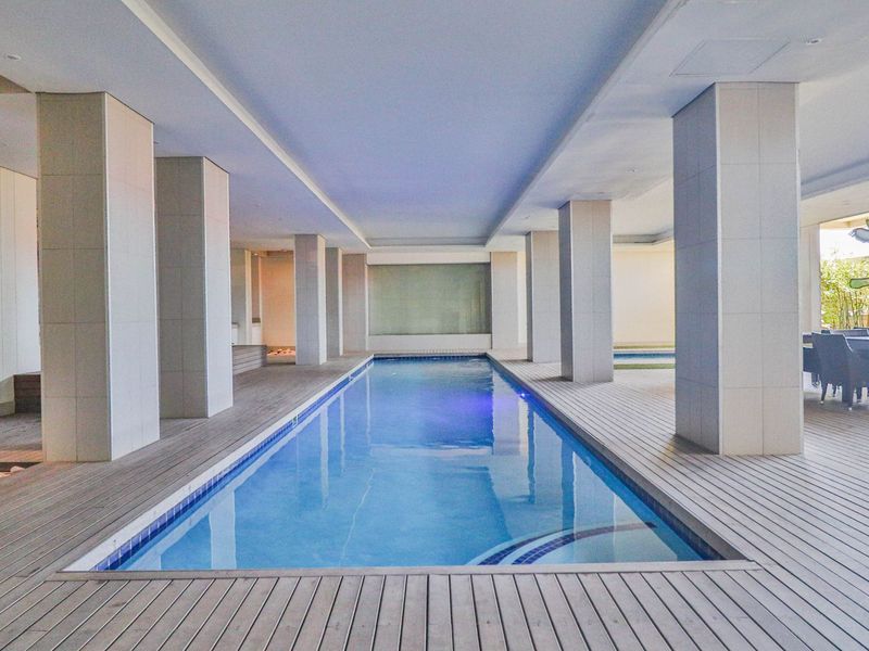 A modern indoor swimming pool area featuring timber decking, structural columns, and recessed lighting, creating a sophisticated and well-maintained communal leisure space.