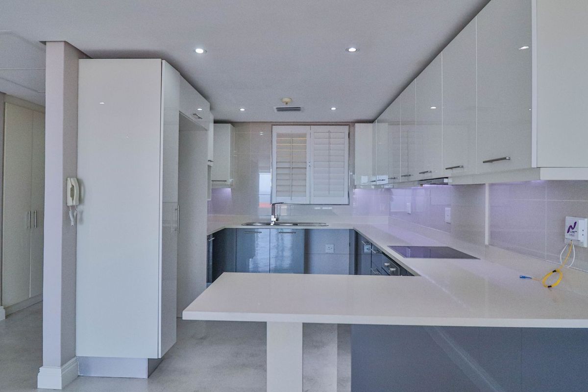 A modern, clean-lined kitchen featuring high-gloss cabinetry, quartz countertops, integrated hob, and recessed lighting in a bright, neutral space.