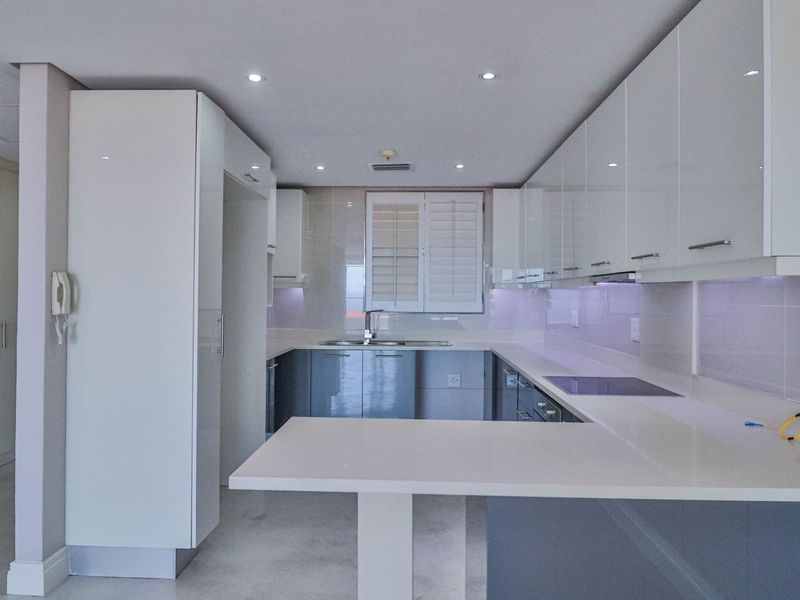 A modern, clean-lined kitchen featuring high-gloss cabinetry, quartz countertops, integrated hob, and recessed lighting in a bright, neutral space.